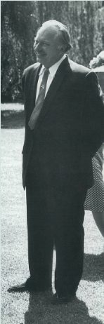 black and white image of LRH wearing a black suit and standing on a lawn.